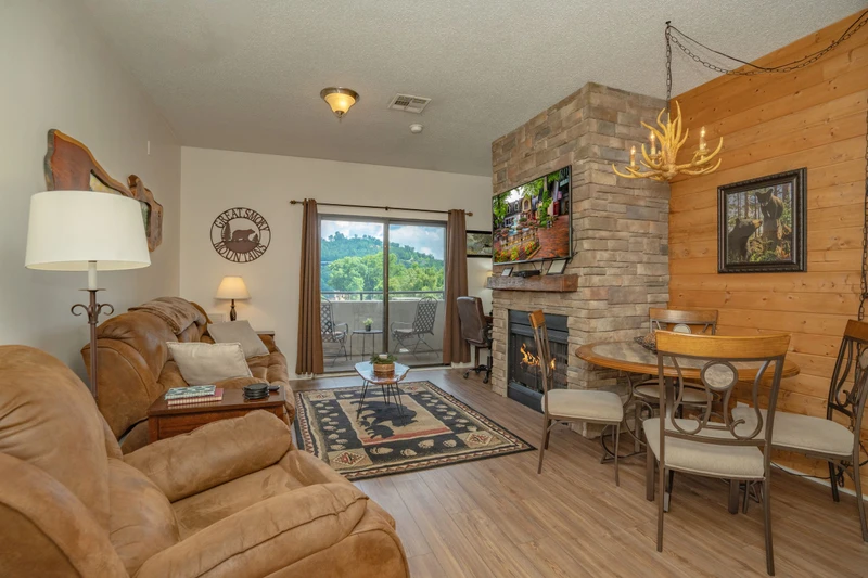 Relax in your cozy living space featuring a stone fireplace, rustic wood accents, and access to your private balcony. The open layout seamlessly connects dining and lounging areas, perfect for unwinding after exploring the mountains.